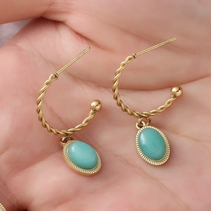 Détail de boucles d'oreilles torsadées dorées avec pierre turquoise ovale en main