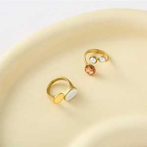 Gold plated oval shell and orange stone rings set on a decorative ceramic tray