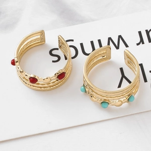 Detail of layered gold stainless steel rings with red and turquoise stone accents