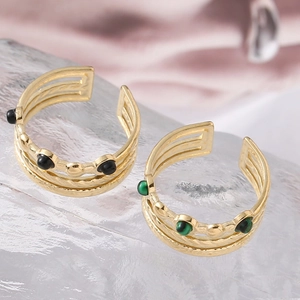 Close-up of gold layered rings featuring black and green beads on a textured surface