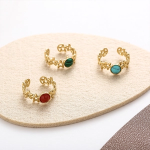 Detail of three gold star rings with red, green, and turquoise stones on felt background