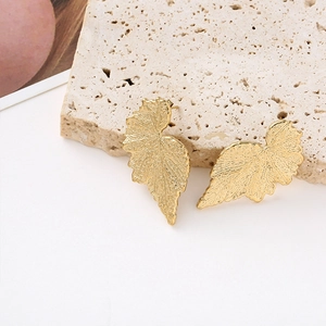 Detailed view of gold leaf earrings with realistic vein texture on beige stone