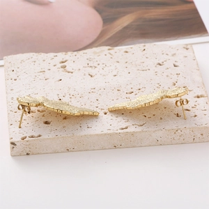 Detailed close-up of gold textured leaf earrings on a beige stone travertine surface