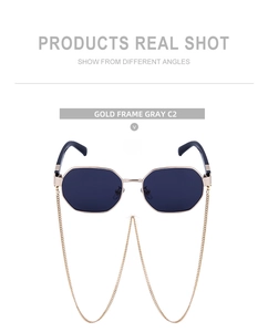 Detail of polygonal sunglasses with gold frame, gray lenses, and detachable metal chain