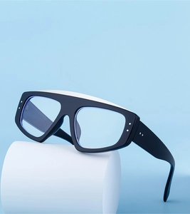 Détail de lunettes de soleil carrées noir mat avec rivets argentés sur fond bleu