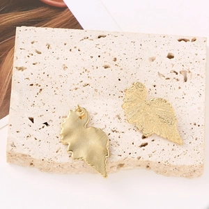 Elegant gold leaf earrings with textured finish on travertine stone display pedestal