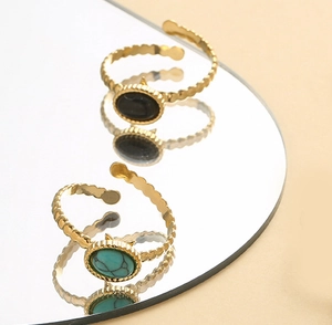 Macro detail of gold-plated wavy rings with black and turquoise oval stones on mirror