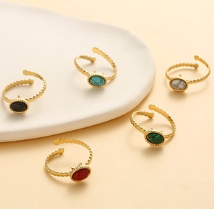 Detail of five gold rings with colorful oval natural stones on ceramic tray