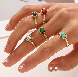 Close-up of five bohemian gold rings set with colorful oval stones on female fingers