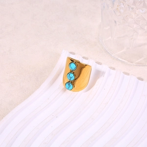 Detail of wide gold ring with three turquoise stones on a white textured background