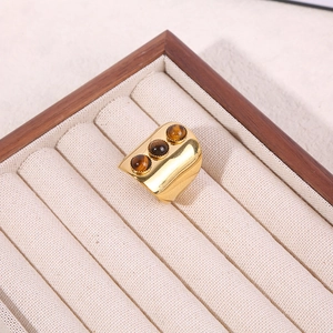 Macro shot of three brown tiger eye stones on a wide gold band ring in a jewelry tray