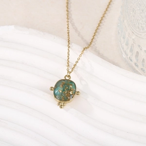 Détail du collier doré avec pendentif ovale vert, incrustation de feuilles d'or et perles
