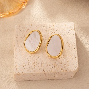 Detail view of oval gold earrings with white marble inlay on a stone pedestal
