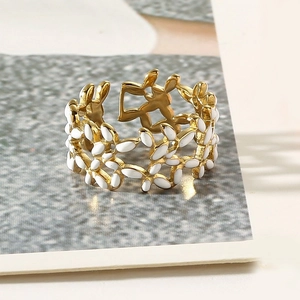Detailed close-up of a gold-plated stainless steel ring with white enamel floral motifs