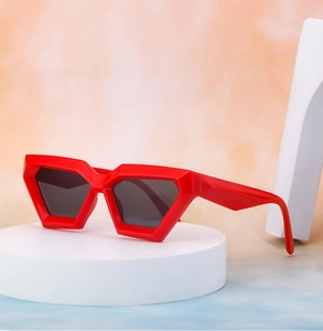 Detail of red geometric cat-eye sunglasses on a white pedestal with vibrant background