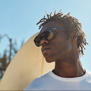 Homme portant des lunettes de soleil carrées noires avec détails argentés sur fond ciel