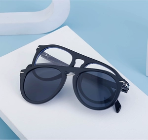 Détail des lunettes de soleil magnétiques noires avec décorations d'ailes sur fond bleu