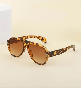 Detail of tortoise shell aviator sunglasses with brown gradient lenses on beige backdrop