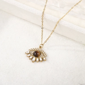 Collier œil maléfique doré avec pierre œil de tigre et cristaux sur fond texturé blanc
