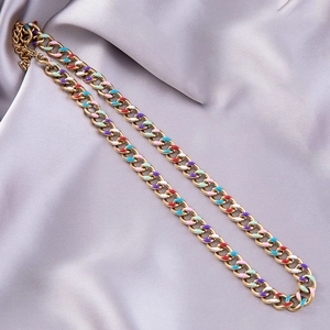 Detail of gold chunky chain necklace with colorful enamel inlay on smooth silk fabric