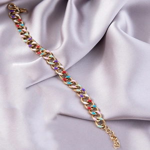 Detailed shot of golden link chain bracelet with colorful enamel charms on silk fabric