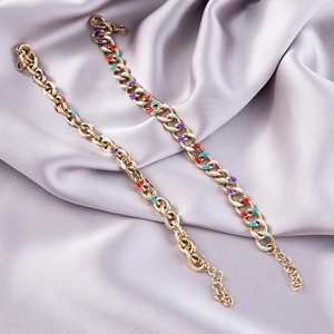 Detail of gold curb chains with multicolored enamel charms on a grey satin background