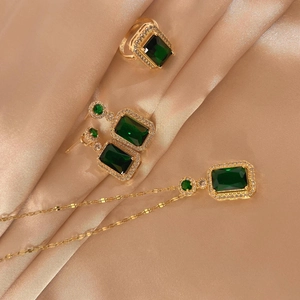 Detailed set of gold titanium jewelry with emerald-cut green gems on champagne satin