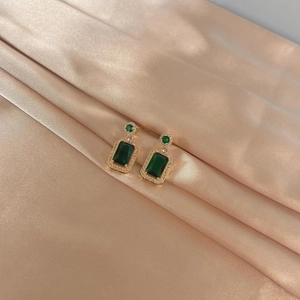 Detailed macro view of emerald green zircon earrings with gold plating on silk fabric