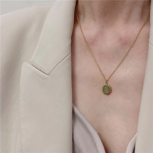 Close-up of a vintage gold necklace with an oval green stone pendant on a beige suit