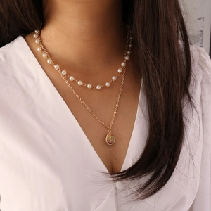 Close-up of a double-layer gold necklace with faux pearls and a teardrop pendant
