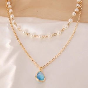 Double-layer gold chain necklace featuring white faux pearls and blue teardrop pendant