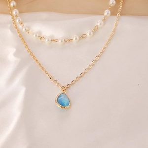 Double-layered gold chain necklace with white pearls and blue teardrop pendant on silk