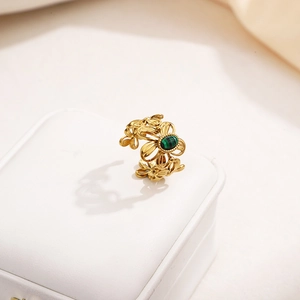Detailed macro view of gold-plated open ring with hollow flower design and green stone