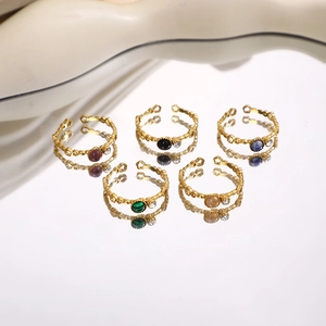 Detailed view of five adjustable gold-plated rings with colorful gemstones on a mirror surface