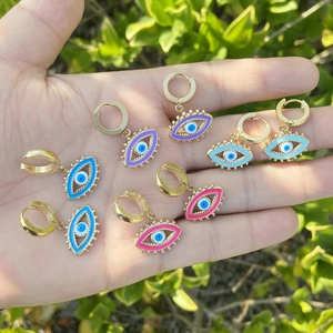 Macro shot of colorful enamel Evil Eye dangle earrings held in hand against green leaves