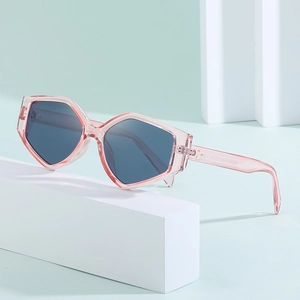Polygonal sunglasses with transparent pink frames and dark gray lenses on a white podium