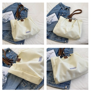 Detailed close-up of beige canvas tote bag with brown leather handles and metal chain