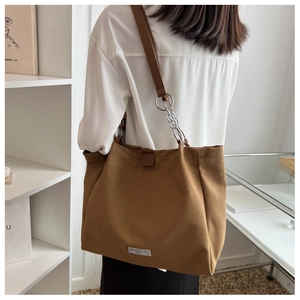 Detail of a large brown canvas tote bag featuring chain straps and a brand label