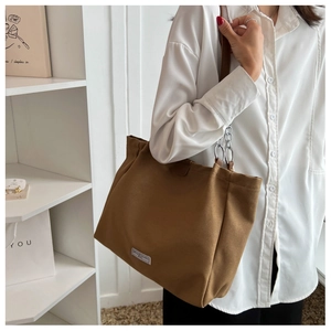 Brown canvas tote bag detail showing the metal chain strap and white brand label