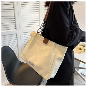 Detail of cream canvas tote bag with brown leather strap and silver chain on model