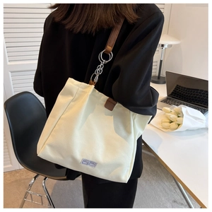 Detail of off-white canvas tote bag with brown leather straps and metallic chain link accents