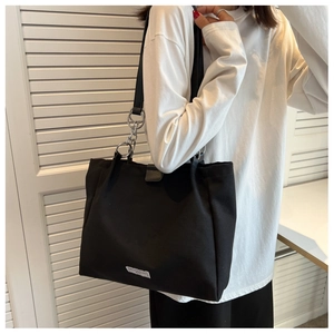 Detail of black canvas tote bag with silver chain strap and minimalist logo label