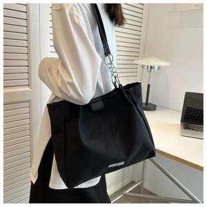 Detail view of a large black tote bag with chain straps shown in an office setting