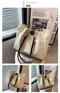 Detail of cream canvas tote bag with brown leather handles and silver metal chains