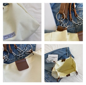 Detail view of canvas tote bag with brown leather accents and silver chain hardware