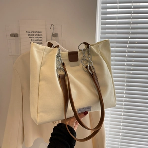 Minimalist canvas tote bag with brown leather handles and silver chain detail in soft light