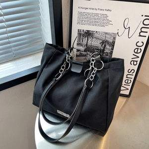 Classic black canvas tote bag with leather straps and silver chain in a minimalist setting
