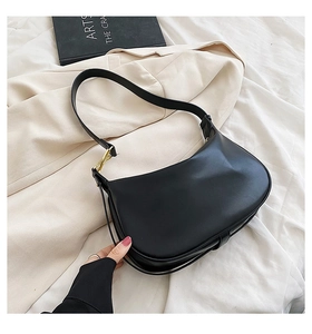 Détail d'un sac hobo noir mat avec boucle dorée sur un fond de tissu beige texturé