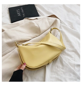 Détail d'un sac à bandoulière jaune vif en forme de croissant sur un fond en tissu beige