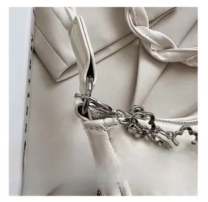 Détail d'un sac à main blanc en cuir avec chaîne florale argentée et anse tressée